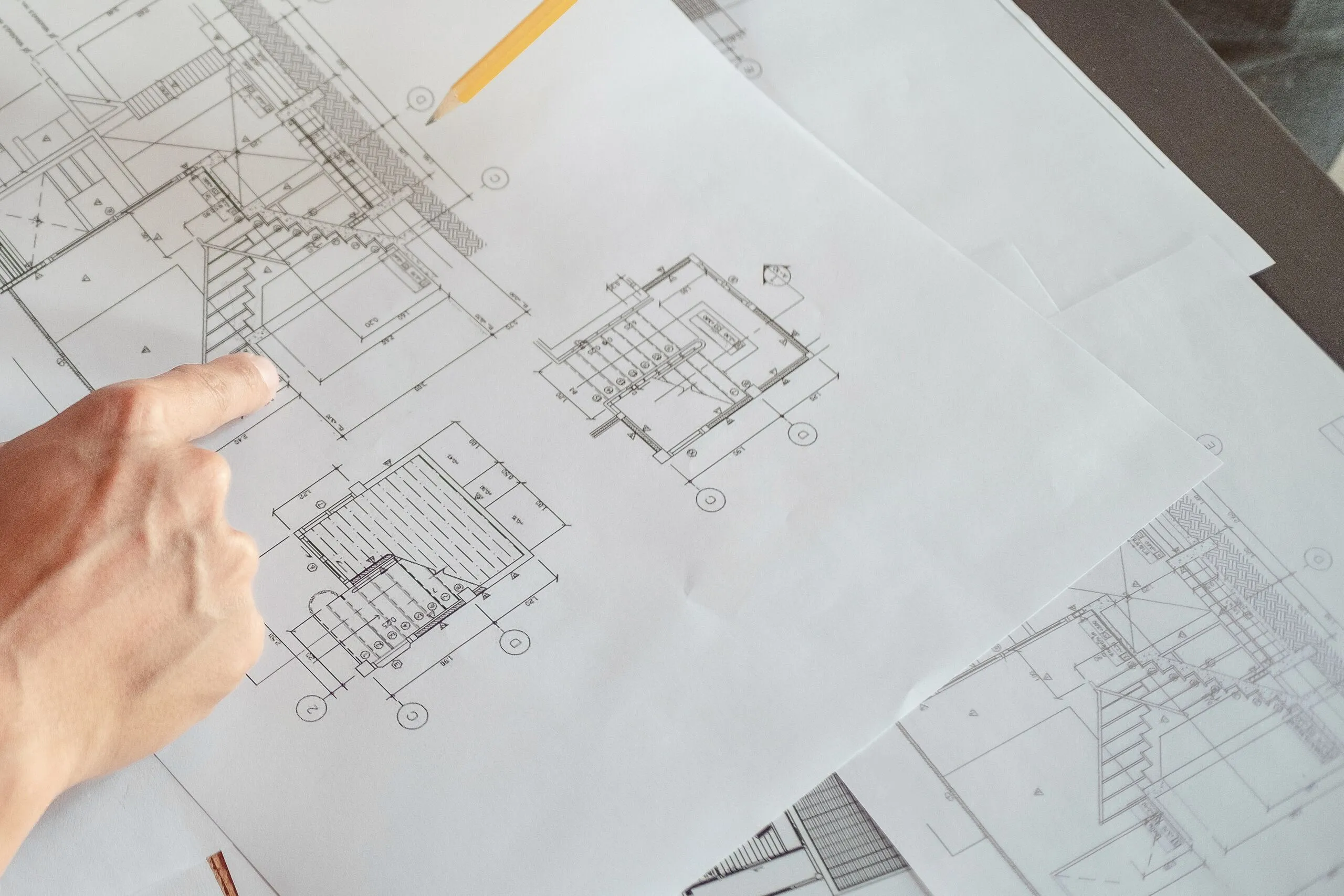 Bauplan auf dem Tisch, eine Hand zeigt auf eine Position im Plan
